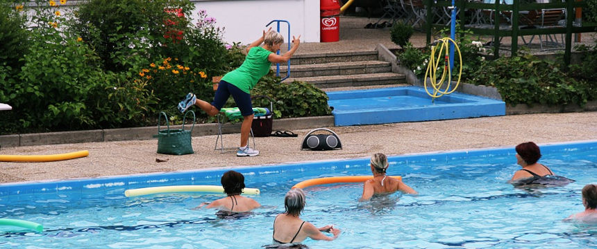 Trainerin zeigt Übung an Land, Teilnehmer im Wasser